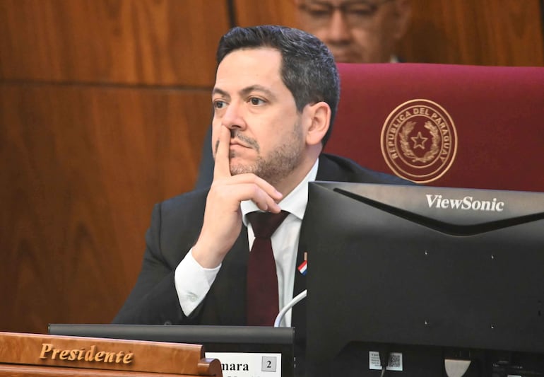 Raúl Latorre Martínez, en traje oscuro y corbata, parece pensativo en reunión formal, con insignia paraguaya visible.