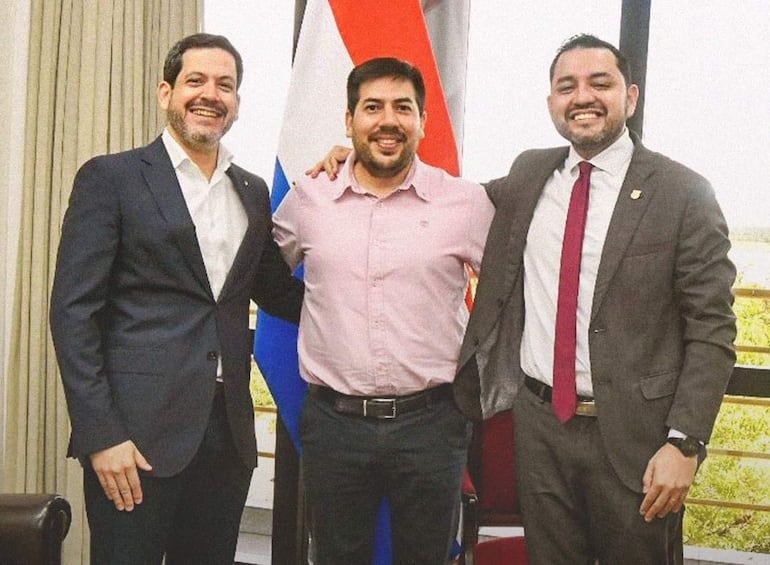 Latorre con saco negro y camisa blanca, Noldin en camisa rosa y Bello en chaqueta gris con corbata roja, todos sonrientes en ambiente iluminado.