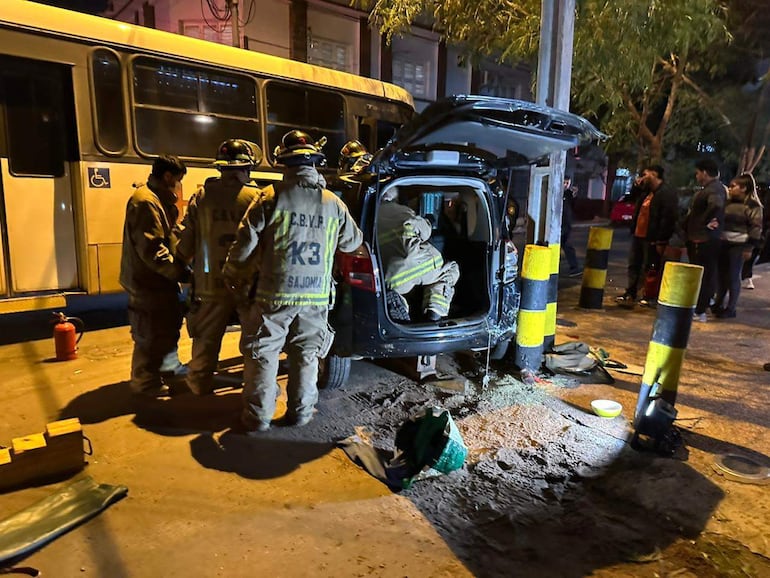 Bomberos con indumentaria en escena nocturna, rodeando un auto con el maletero abierto y un extintor visible en el suelo.