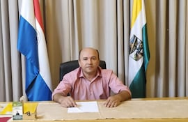 Ramón Sanabria sentado en un escritorio, vistiendo camisa rosa, con banderas de Paraguay y otra detrás.