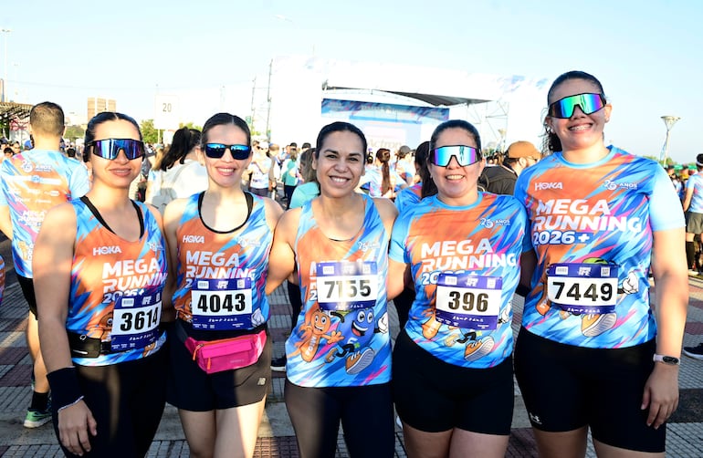 Cinco mujeres sonrientes en camisetas coloridas de 'MEGA RUNNING 2026', preparándose para la carrera en un ambiente deportivo.