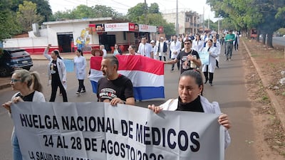 Grupo de médicos en bata blanca marchando, sosteniendo carteles con el lema 'Huelga Nacional de Médicos'.