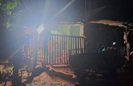 Casa de madera iluminada en entorno rural, con un vehículo de tres ruedas estacionado frente a la entrada y vegetación alrededor.