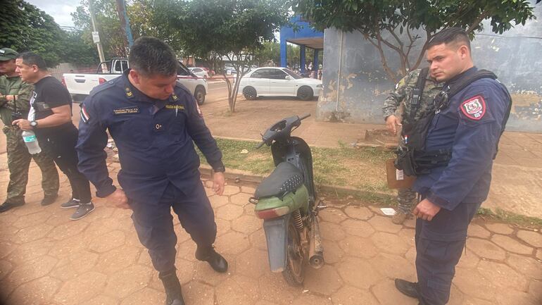 Suboficiales policiales en uniforme azul inspeccionan una moto mientras un hombre observa desde la distancia en un entorno urbano.