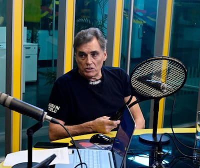 Víctor Pecci sentado en un estudio de radio, vistiendo camiseta negra con la palabra 'REBEL', hablando con gestos expresivos.