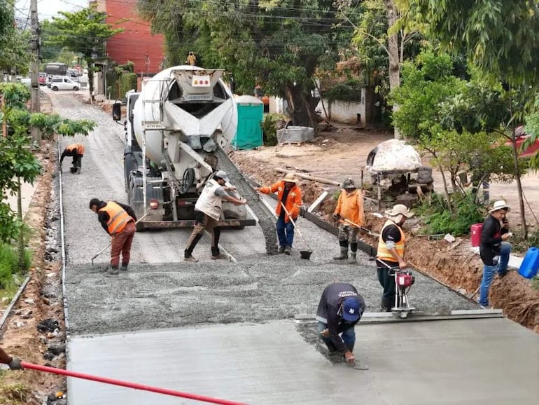 Grupo de seis trabajadores en chalecos de seguridad, utilizando herramientas y hormigonera en obra de desagüe, bajo un ambiente soleado.