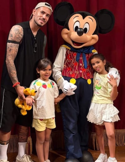 Antonio Sanabria, con tatuajes, posa en el centro rodeado de tres niñas sonrientes en un ambiente temático de Disney.