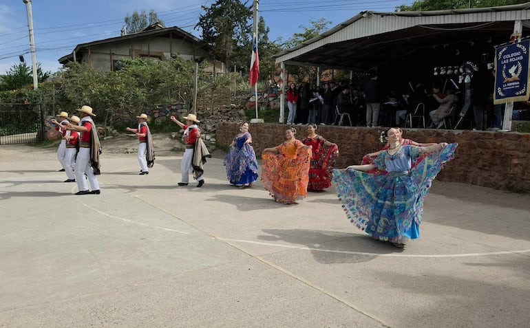 Bailarines en vestimenta tradicional roja y blanca y mujeres en vestidos coloridos, disfrutando de una danza folclórica en un ambiente escolar.