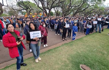 Mujeres con carteles que indican grados escolares entre un grupo numeroso de estudiantes al aire libre en un ambiente tranquilo.