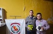 Concejales Pablo Callizo en sudadera gris y Sebastián Garay en camisa a cuadros, serios, sosteniendo muñecos de peluche en comisaría amarilla.