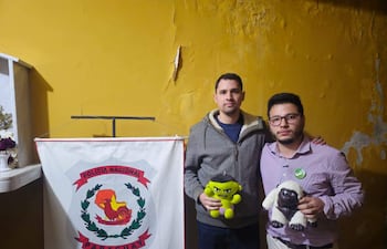 Concejales Pablo Callizo en sudadera gris y Sebastián Garay en camisa a cuadros, serios, sosteniendo muñecos de peluche en comisaría amarilla.