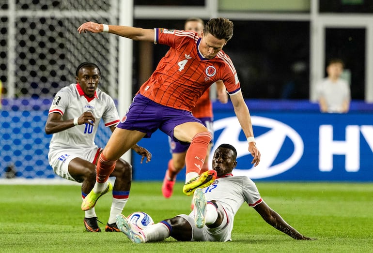 El haitiano Danley Jean Jacques se arroja y despoja del balón al mediocampista escocés Scott McTominay, mientras observa atrás el caribeño Jean-Ricner Bellegarde (10).