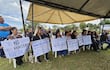 Grupo de manifestantes bajo carpa, hombres y mujeres sosteniendo carteles de protesta sobre el cambio de sentido de calles.