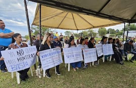 Grupo de manifestantes bajo carpa, hombres y mujeres sosteniendo carteles de protesta sobre el cambio de sentido de calles.