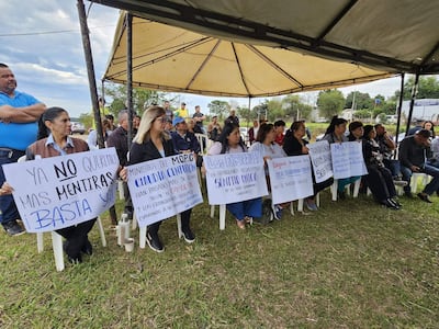 Grupo de manifestantes bajo carpa, hombres y mujeres sosteniendo carteles de protesta sobre el cambio de sentido de calles.