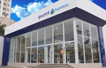 Fachada moderna de la farmacia 'Punt Farma', con amplios ventanales y escaleras de acceso, en un entorno urbano.