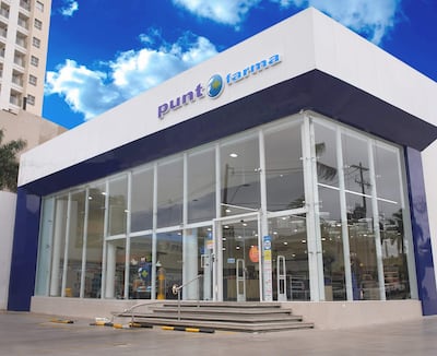 Fachada moderna de la farmacia 'Punt Farma', con amplios ventanales y escaleras de acceso, en un entorno urbano.