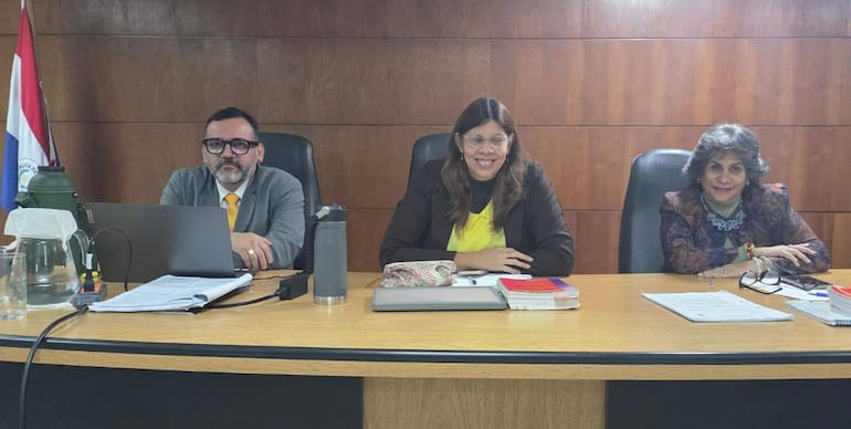 Fabián Weisensee en gafas y corbata amarilla, Laura Ocampo sonriente en blusa amarilla y otra mujer con chaqueta oscura, en un ambiente formal.