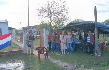 Grupo de padres y niños, con una mujer en abrigo claro al frente, y un soldado vigilando en uniforme camuflado.