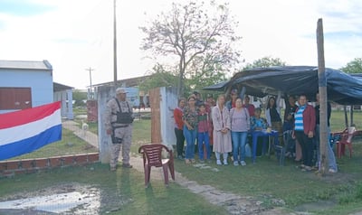 Grupo de padres y niños, con una mujer en abrigo claro al frente, y un soldado vigilando en uniforme camuflado.