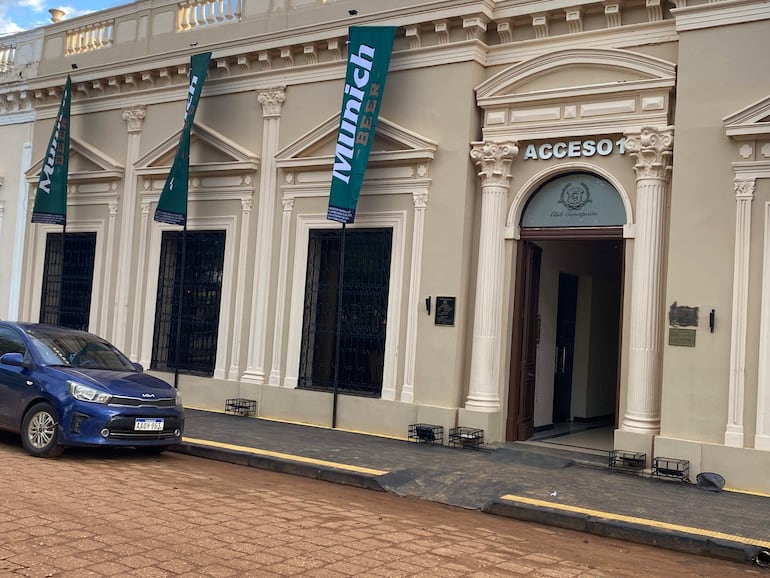 Edificio del Club Concepción con banderas ondeando y un coche azul estacionado al lado.