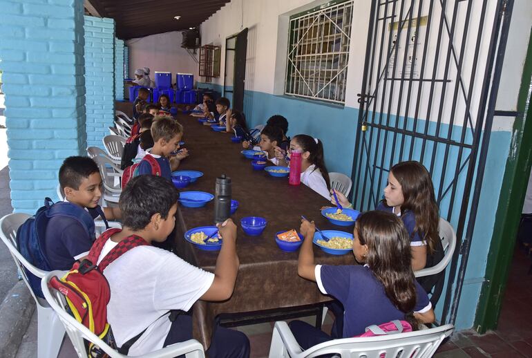 Niñas y niños almuerzan en un pasillo, sin ventiladores, ante la falta de comedor en la escuela Juan Manuel Frutos, de Barrio Obrero.