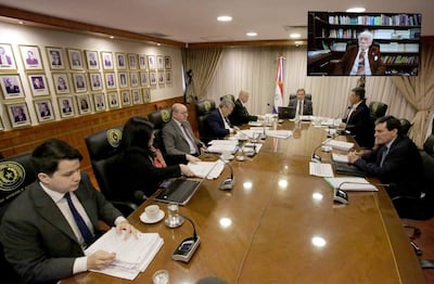Siete personas en traje formal discuten alrededor de una mesa ovalada. Bandera de Paraguay en el fondo y documentos sobre la mesa.