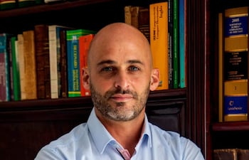 Manuel Guanes Nicoli, de pie con camiseta azul clara, frente a estantería repleta de libros, con expresión tranquila.