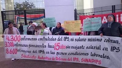 Marina Ayala y otras mujeres sostienen pancartas en protesta frente al IPS, transmitiendo mensajes sobre condiciones laborales.