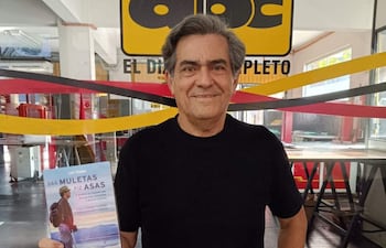 Luiz Thadeu con camiseta negra sonríe mientras sostiene su libro en un ambiente decorado en rojo y amarillo.