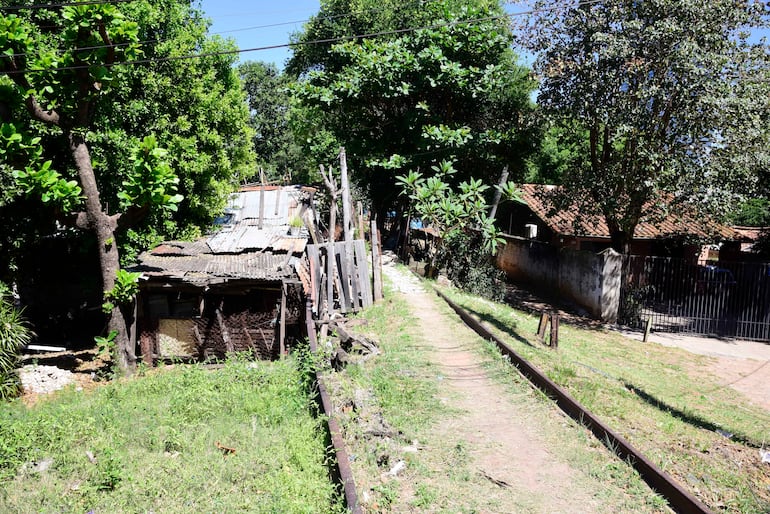Entorno rural con vía de tren, vegetación densa y edificaciones deterioradas en un área deshabitada.