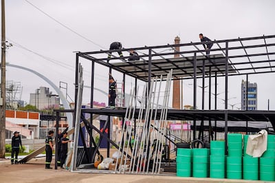 Seis trabajadores en uniformes oscuros con detalles verdes, montando una estructura metálica en un ambiente urbano con materiales de construcción.