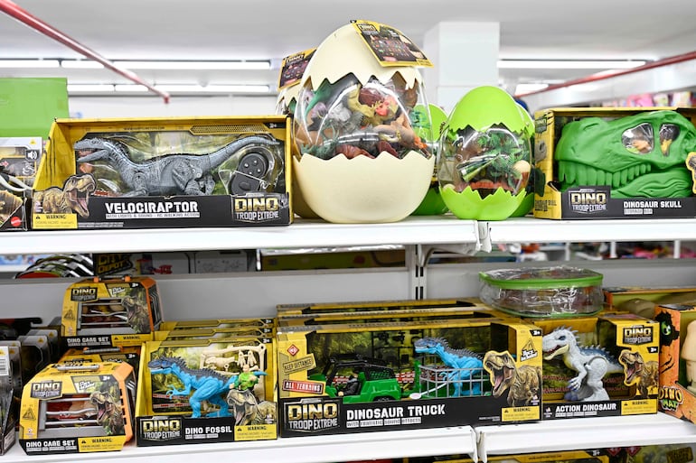 Estante lleno de juguetes coloridos de dinosaurios, incluyendo un velociraptor y un camión, en un ambiente de tienda de juguetes.