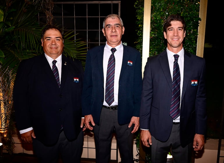 Francisco Gómez sonriente en traje oscuro, junto a otros hombres en un evento formal al aire libre rodeado de vegetación.