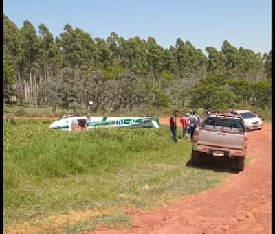 Grupo de hombres examinando una aeronave averiada, rodeados de vegetación, con un vehículo de doble cabina estacionado.