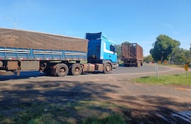 Dos camiones de carga en carretera, uno en movimiento, vegetación al fondo bajo un cielo azul.