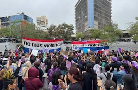 Multitud de mujeres con pañuelos morados y cartel que dice 'no más violencia', manifestándose en un ambiente urbano.
