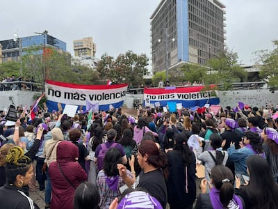 Multitud de mujeres con pañuelos morados y cartel que dice 'no más violencia', manifestándose en un ambiente urbano.