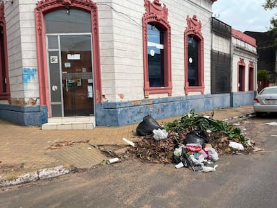 Montón de basura en la acera frente a edificio con detalles en rosa, sin personas visibles en el entorno urbano.
