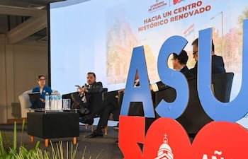 Luis Bello en traje oscuro, gesticulando mientras habla en un panel. Ambiente moderno con plantas decorativas y pantalla al fondo.