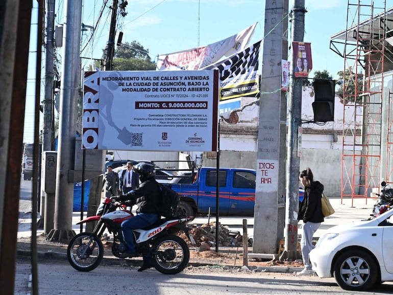 Escena urbana en Asunción con una persona en motocicleta y vehículos, y un cartel de obra vial al fondo.