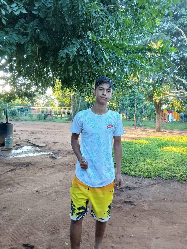 Adolescente con camiseta blanca y shorts amarillos, sonríe con el pulgar hacia arriba en un entorno verde, con árboles y césped.
