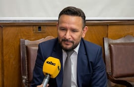 Derlis Léon con barba y traje oscuro, sosteniendo un micrófono amarillo en un espacio con paredes de madera.