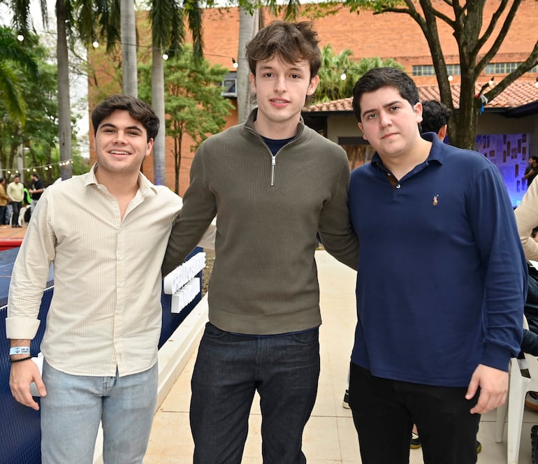 Tres jóvenes, felices y tranquilos, posando juntos: uno con camisa clara, otro con prenda oscura y el tercero con camiseta azul marino.