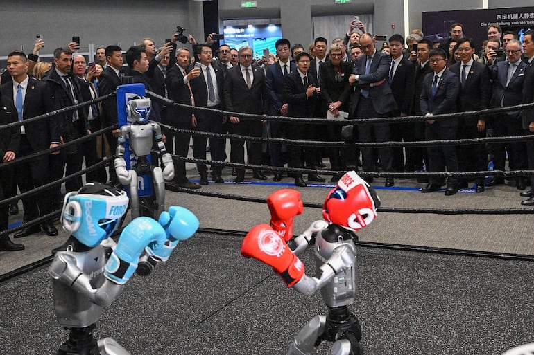 El canciller alemán Friedrich Merz (atrás, centro derecha), acompañado por el CEO de Unitree Robotics, Wang Xingxing (atrás, centro izquierda), observa una exhibición de boxeo entre robots en una sala de exposición de productos de Unitree Robotics en Hangzhou, en la provincia oriental china de Zhejiang, el 26 de febrero de 2026.
