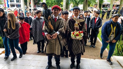 Dos jóvenes sostienen estatuas en el centro de una procesión frente a la Parroquia de W Sonta Cro, luciendo vestimenta tradicional.