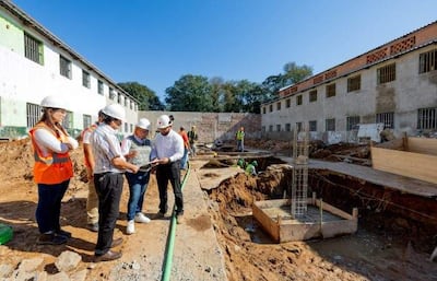 Mujer con casco naranja observa mientras hombres revisan documentos en un sitio de construcción bajo un cielo claro.