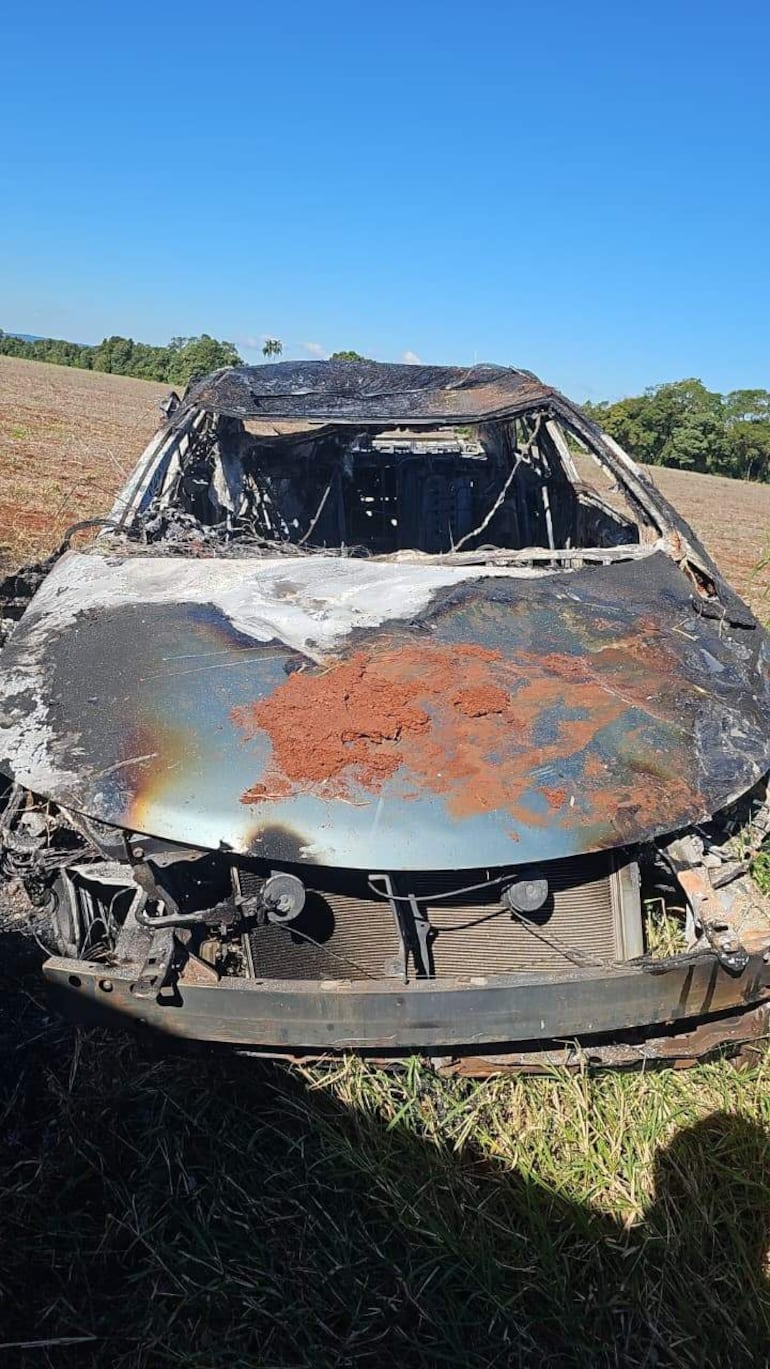 Vehículo incinerado en campo con daños severos y terreno cubierto de tierra en un día despejado.