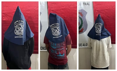 Tres hombres en capuchos azules de la Comisaría 10ª Central, de espaldas, en un entorno policial con fondo rojo.