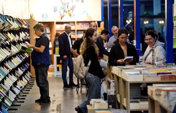 Hombres y mujeres visitan la feria, observando libros en un ambiente acogedor, con luces cálidas y estanterías repletas.